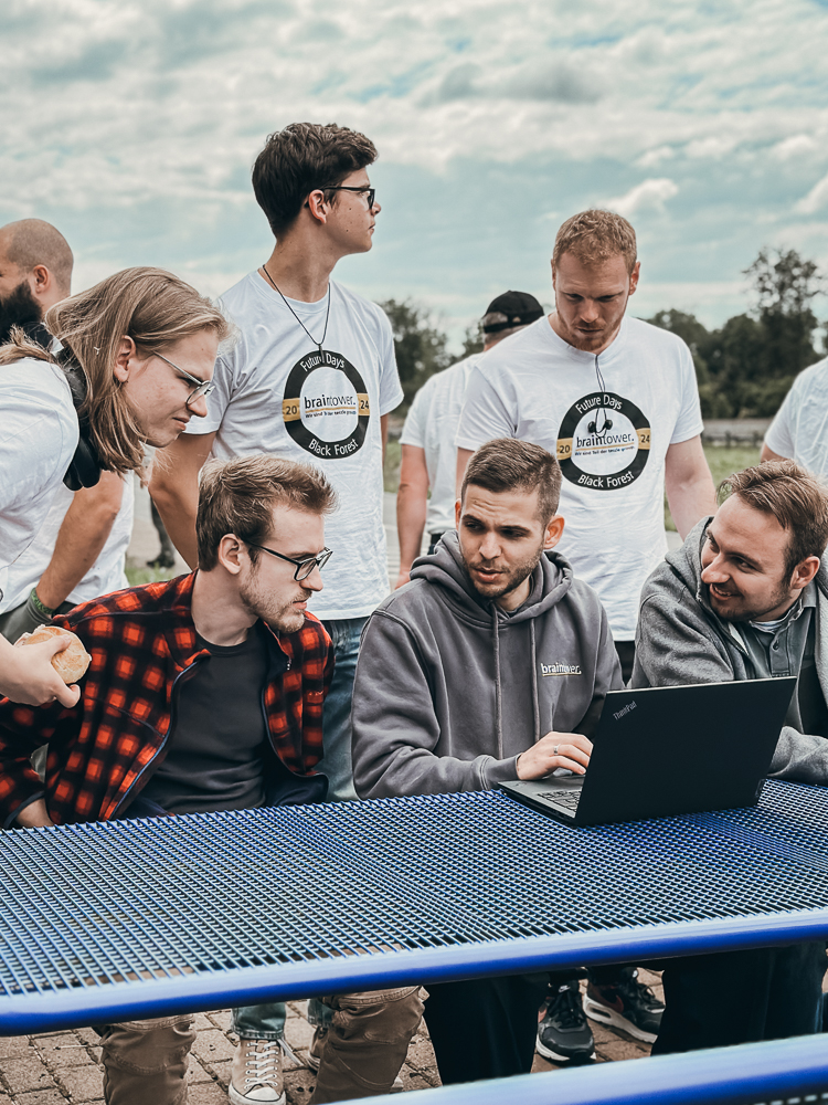 Mitarbeiter von Braintower bei den Future Days 2024 im Schwarzwald, arbeiten im Freien zusammen an einem Laptop